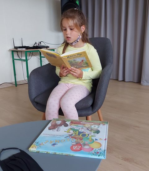 dziewczynka siedzi w fotelu, w rękach trzyma otwartą książkę, czyta