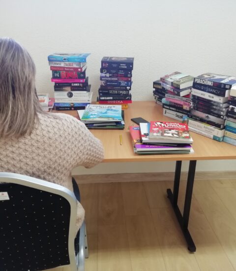 kobieta siedzi tyłem na krześle przy stole, na którym ułożone są książki