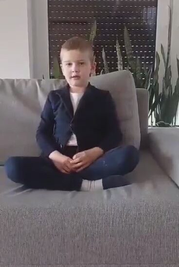 chłopiec ubrany w szarą marynarkę i ciemne spodnie, siedzi na kanapie