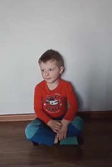 chłopiec siedzi na podłodze, ubrany w czerwoną bluzkę