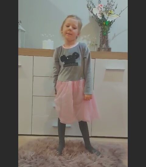 dziewczynka w sukience stoi na dywanie, w tle jasne meble