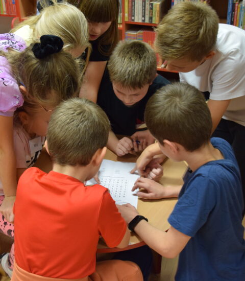 grupa dzieci pochylona nad stołem, rozwiązują zagadkę