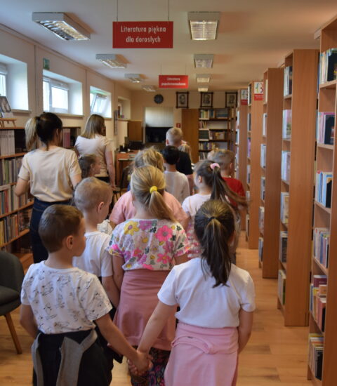 dwie kobiety i grupa dzieci idą przez bibliotekę