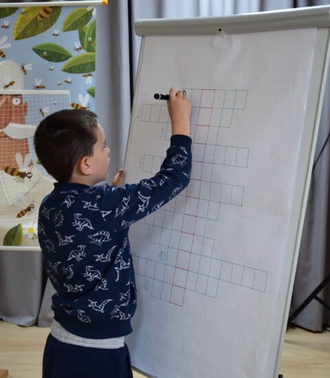 chłopiec pisze na tablicy, w tle plansza edukacyjna