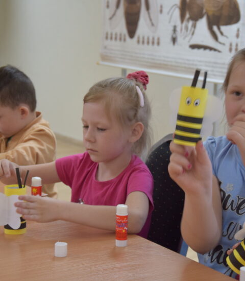 dwie dziewczynki i dwóch chłopców siedzą przy stole, kleją papierowe pszczoły