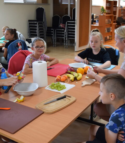 kobiety z małymi dziećmi siedzą przy stole, kroją owoce