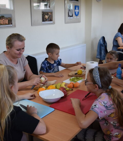 kobiety z małymi dziećmi siedzą przy stole, kroją owoce