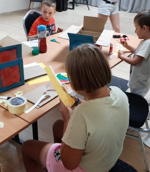 dzieci siedzą przy stołach, kleją, wycinają, malują kartonowe pudełka