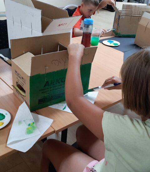 dziewczynka maluje zieloną farbą kartonowe pudełko