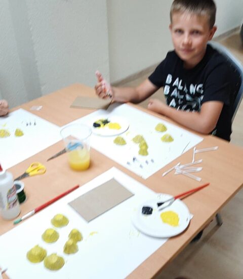 dwóch chłopców siedzi przy stole, malują żółtą farbą