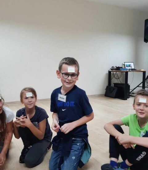 dzieci siedzą na podłodze, do czola maja przyklejone karteczki