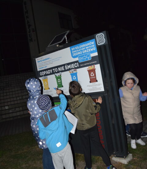 czworo dzieci stoi przy tablicy informacyjnej dotyczącej segregacji śmieci