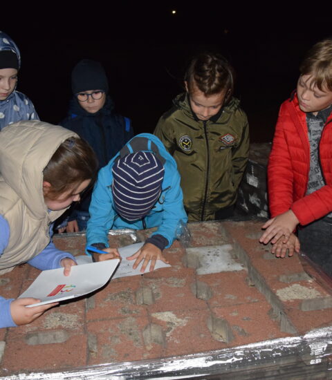 noc, kilkoro dzieci stoi przy kostce brukowej ułożonej na palecie, chłopiec coś zapisuje