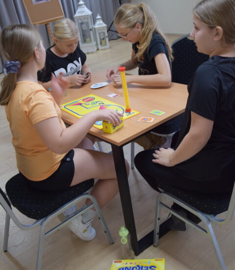 cztery dziewczyny siedzą przy stoliku, rozłożoną maja grę planszową