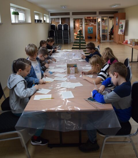 grpa dzieci siedzących przy stole przykrytym folią, każdy skupiny na swojej pracy, wycinają coś z papieru