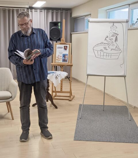 pisarz trzyma otwartą książkę, obok tablica z rysunkiem