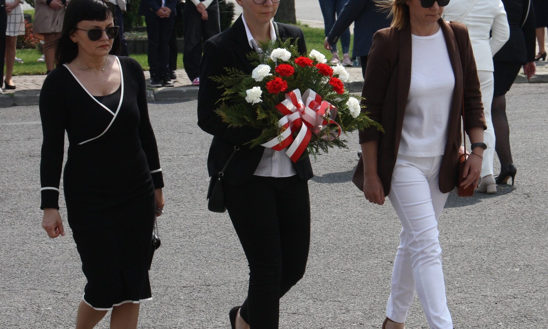trzy kobiety idą, jedna trzyma wiązankę kwiatów