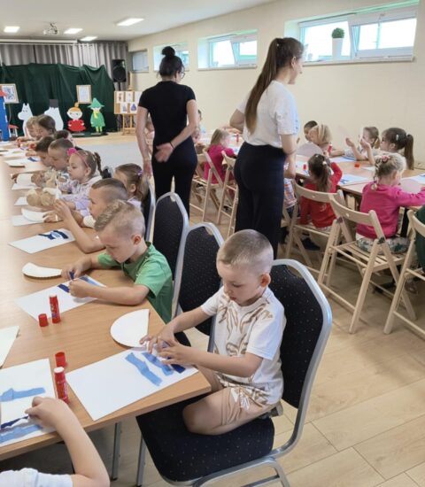 dzieci siedzą przy stołach, wyklejają