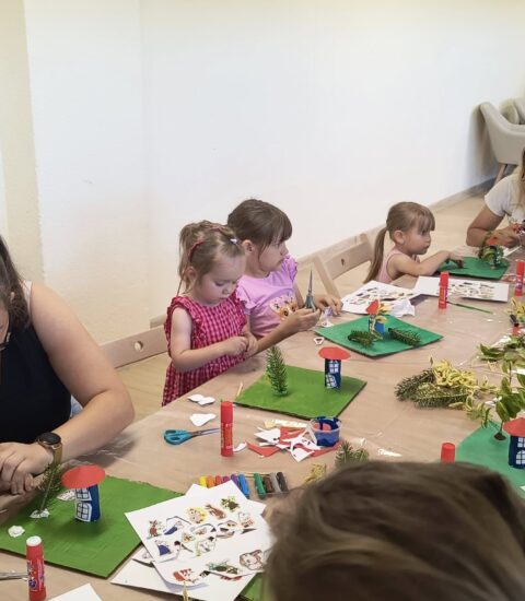 uczestnicy zajęć podczas wakacji, wykonuja prace plastyczne siedząc przy stołach