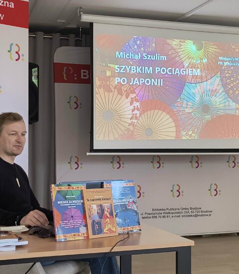 mężczyzna siedzi przy stoliku, w tle ekran, na ktorym wyświetlany jest kolorowy obraz