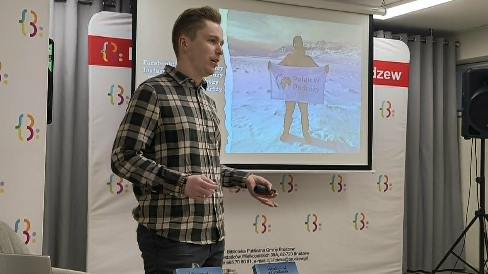 mężczyzna w koszuli w kratę stoi na tle ekranu, na którym wyświetlana jest prezentacja o Grenlandii