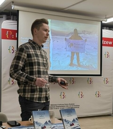 mężczyzna w koszuli w kratę stoi na tle ekranu, na którym wyświetlana jest prezentacja o Grenlandii
