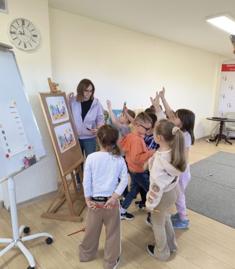 kobieta i grupka dzieci stoją przy sztaludze, podnoszą ręce