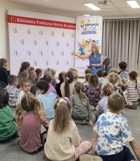autorka siedzi w fotelu przed dziećmi, ręką wskazuje na dzieci