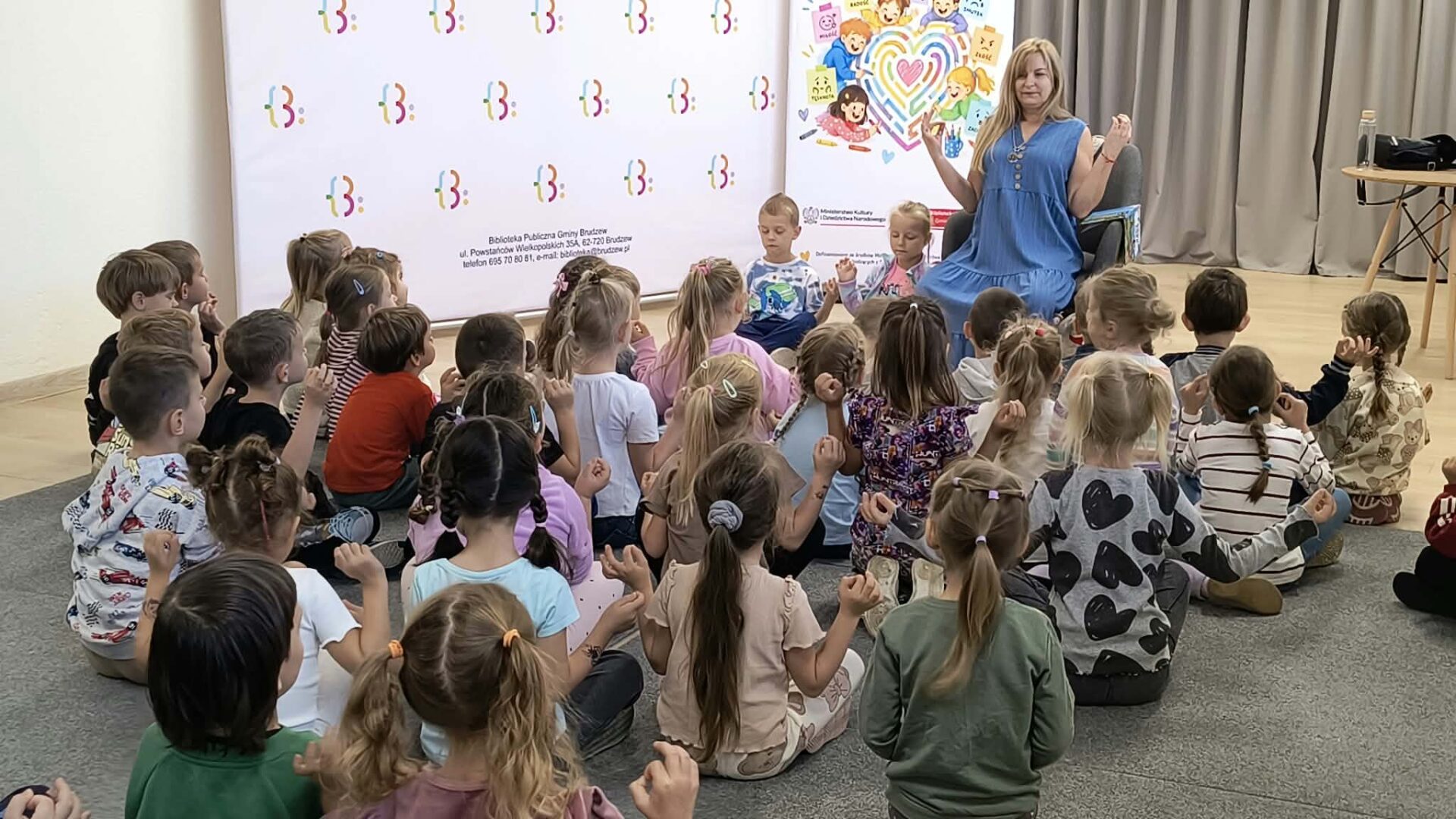 autorka siedzi w fotelu przed dziećmi, ma podniesione ręce