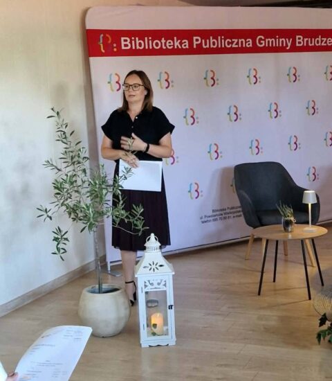kobieta stoi na tle ścianki, mówi do publiczności