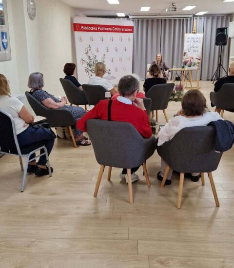 uczestnicy spotkania , w tle autorka siedząca przy stoliku