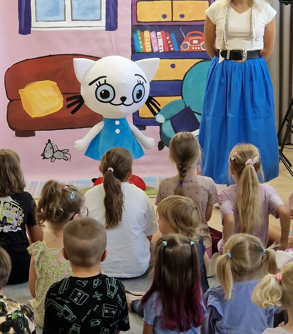 maskotka kotki, obok stoi kobieta w niebieskiej spódnicy