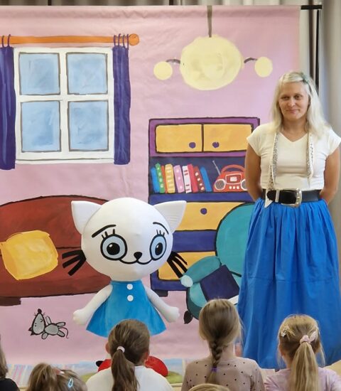 maskotka kotki, obok stoi kobieta w niebieskiej spódnicy